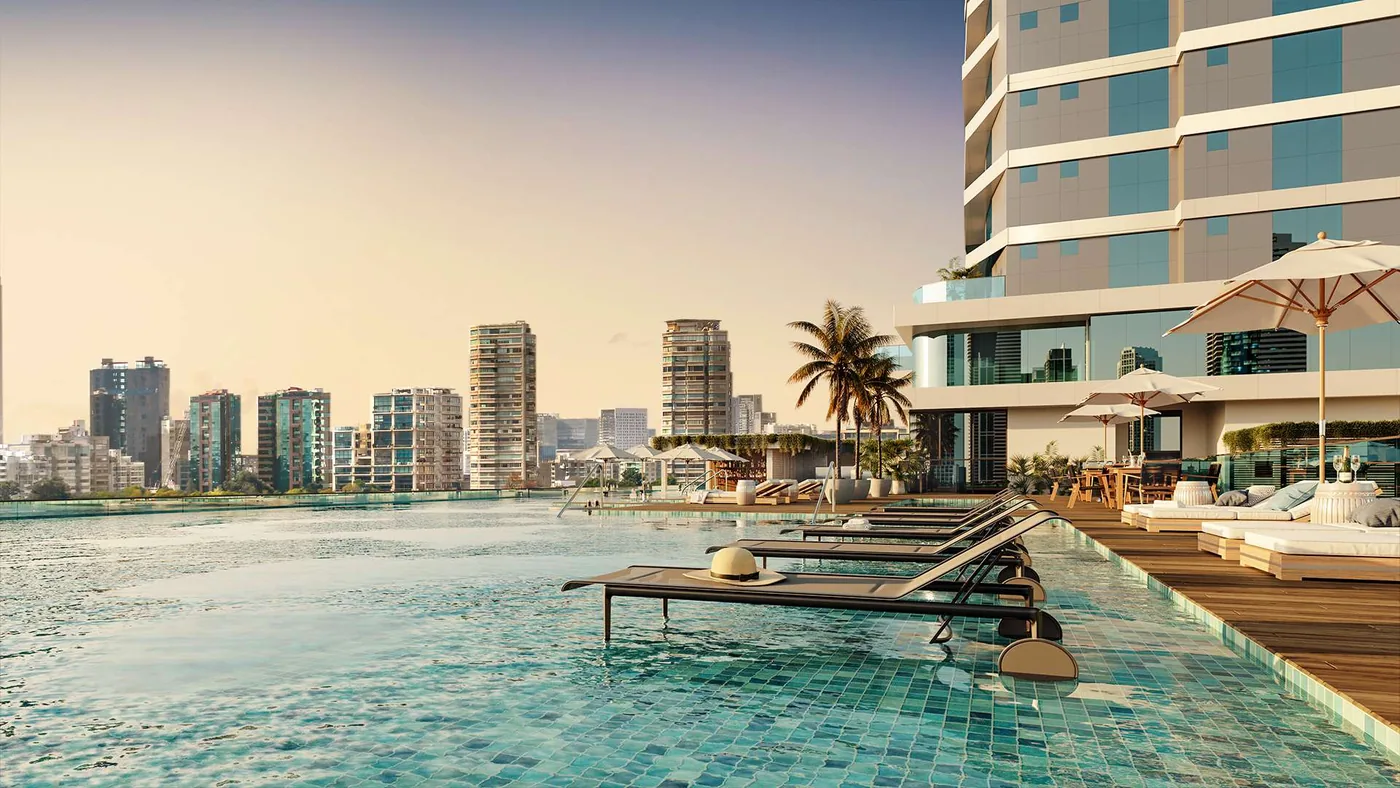 Piscina na borda do pavimento de lazer, com espreguiçadeiras dentro da lâmina de água e o skyline de Balneário Camboriú ao fundo