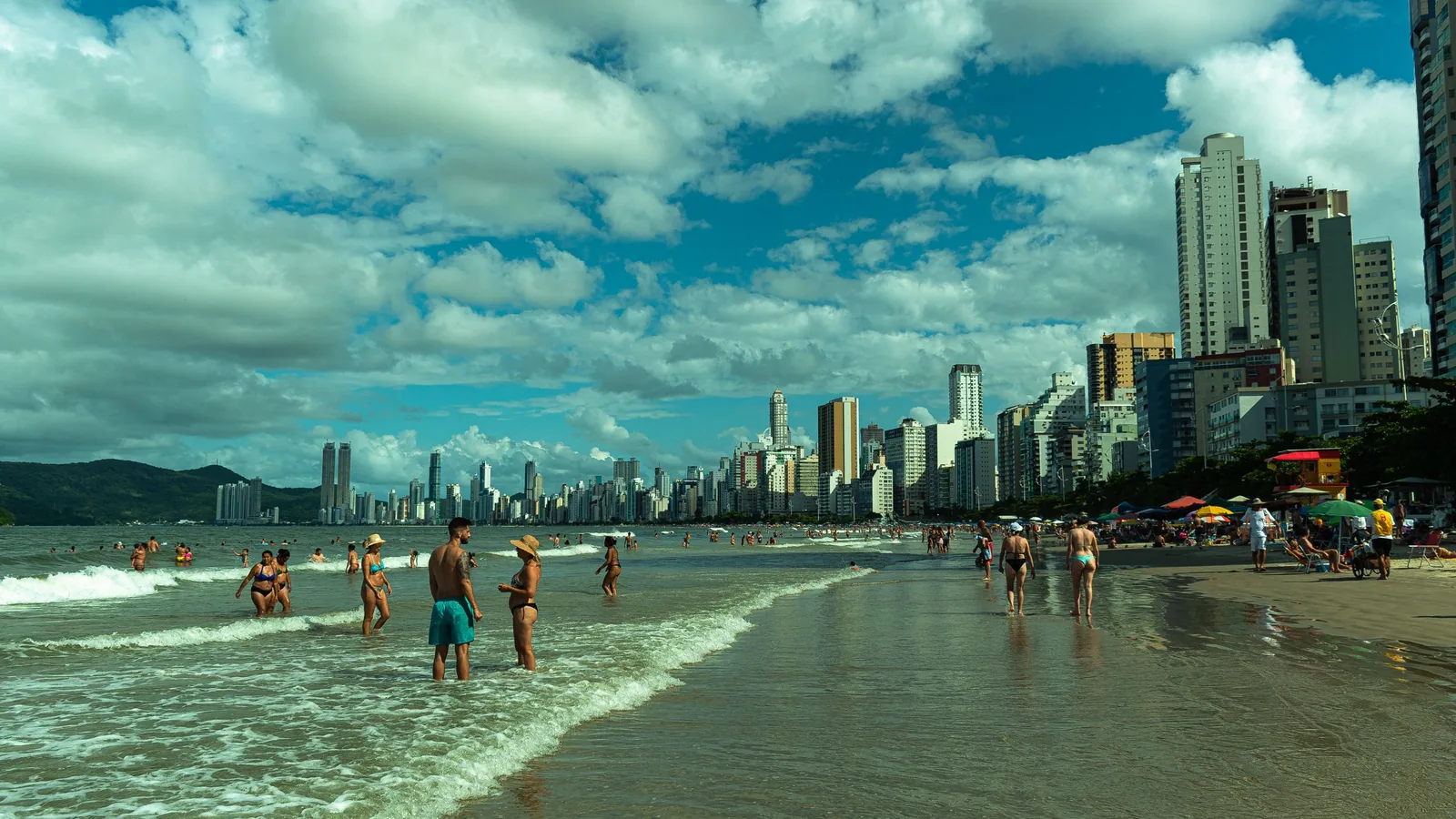 Beira-mar de Balneário Camboriú em dia de sol, com banhistas na água e os arranha-céus da orla ao fundo