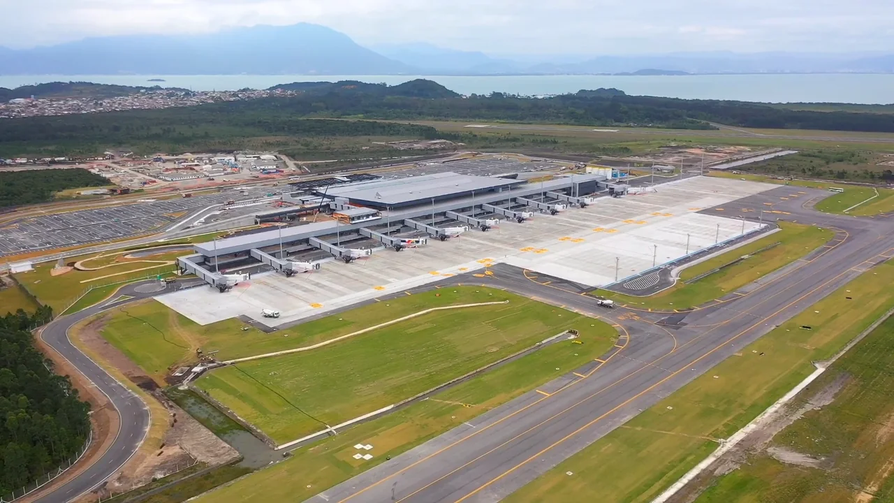Vista aérea do terminal do aeroporto de Florianópolis, com a pista em primeiro plano e a baía e as montanhas ao fundo