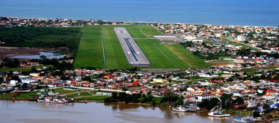 Vista aérea da pista do aeroporto de Navegantes, cercada de campos verdes e do casario da cidade