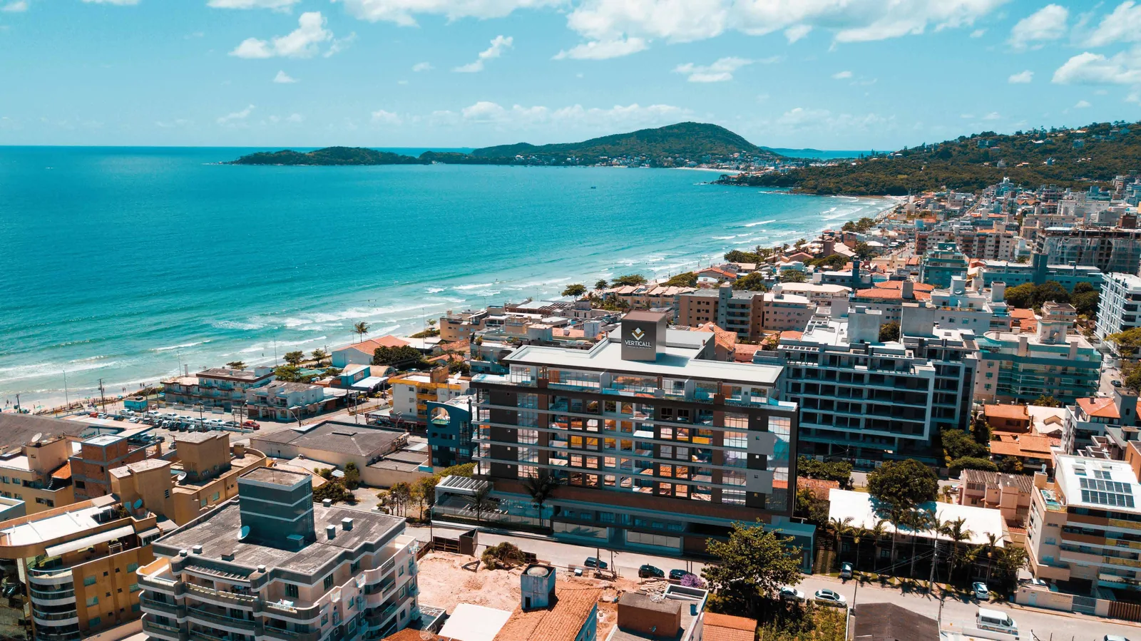 O bairro visto de cima, com as quadras de casas e prédios baixos entre o morro e a praia
