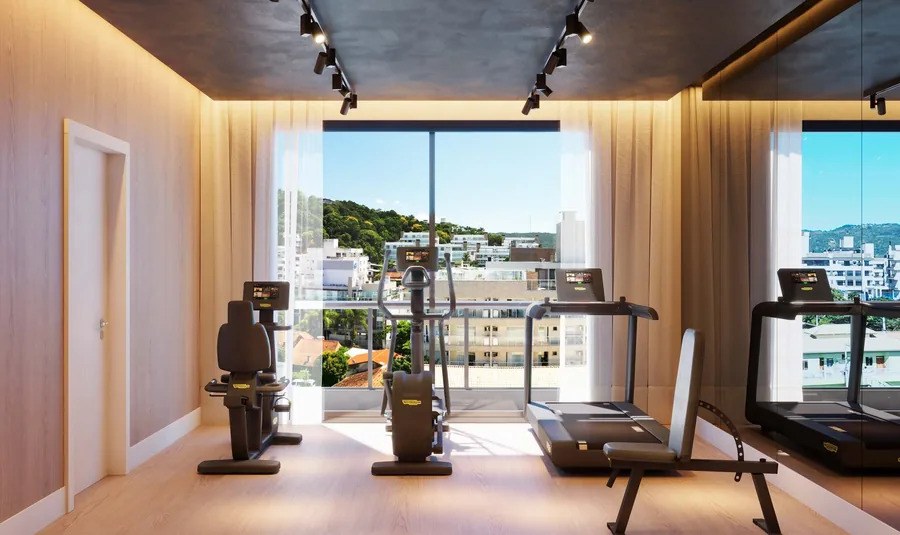 Academia com esteiras e aparelhos de musculação diante de janelas do piso ao teto, com vista para os prédios baixos do bairro