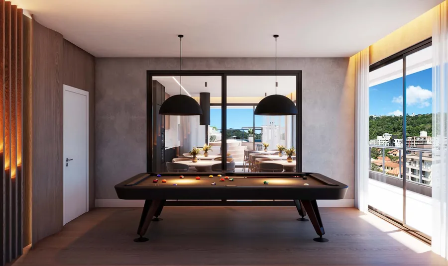 Sala de jogos com mesa de sinuca ao centro, dois pendentes de cúpula preta, parede de concreto aparente e janela para o morro