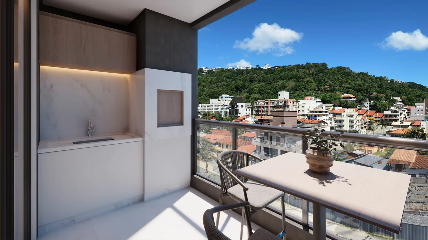 Sacada do apartamento com a churrasqueira a carvão embutida na parede, mesa redonda para dois e vista para as casas e o morro verde