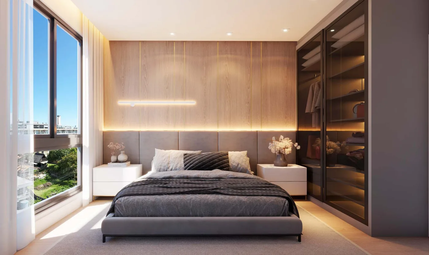 Suíte com cabeceira de madeira iluminada por trás, cama de casal, closet de vidro fumê à direita e janela alta para o bairro