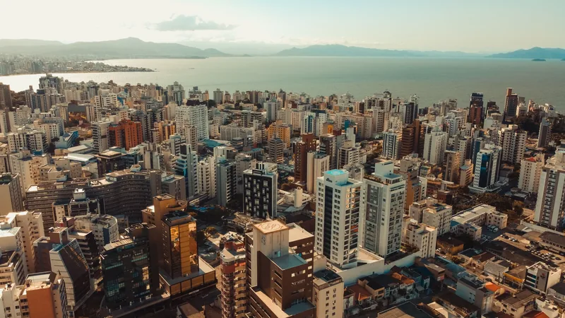 Vista aérea de Florianópolis ao fim da tarde, com os prédios da cidade e a baía ao fundo