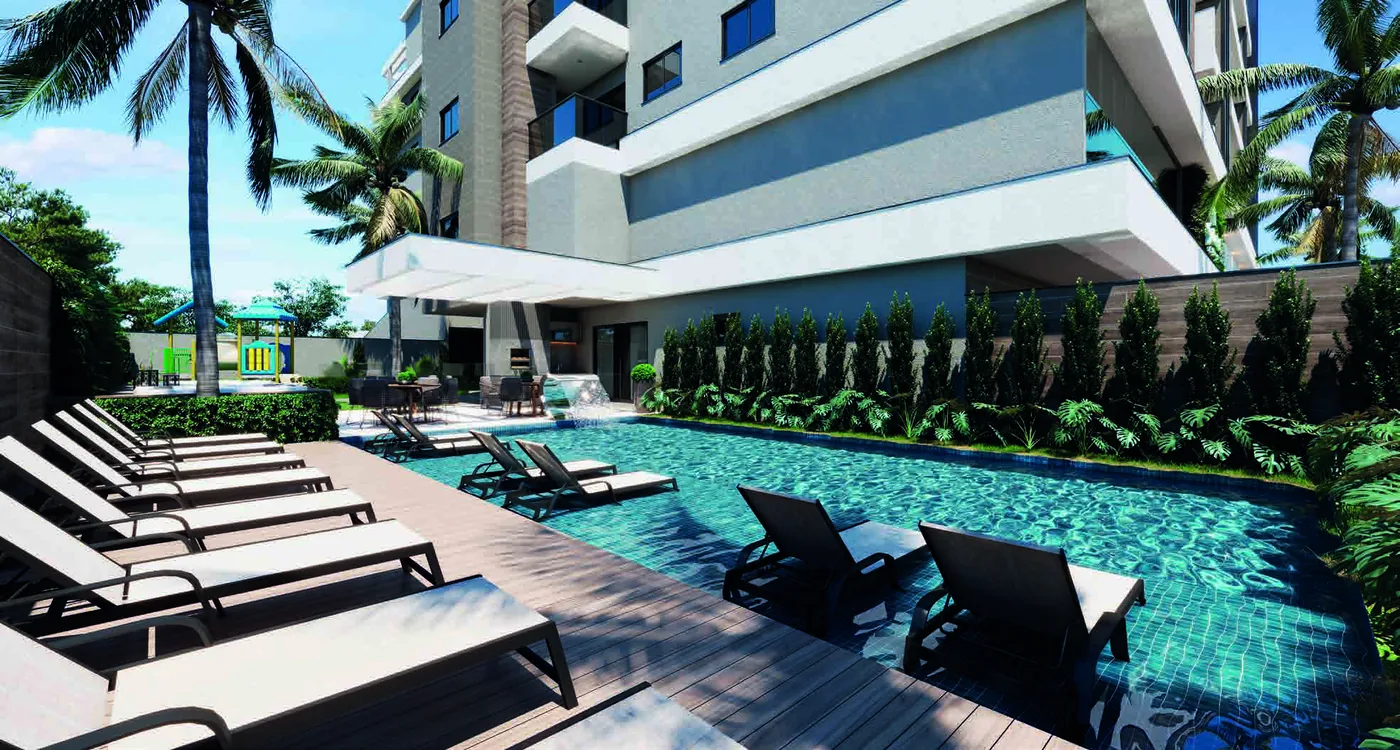 Piscina ao ar livre com deck de madeira, espreguiçadeiras alinhadas, muro de vegetação e o prédio subindo ao fundo entre coqueiros