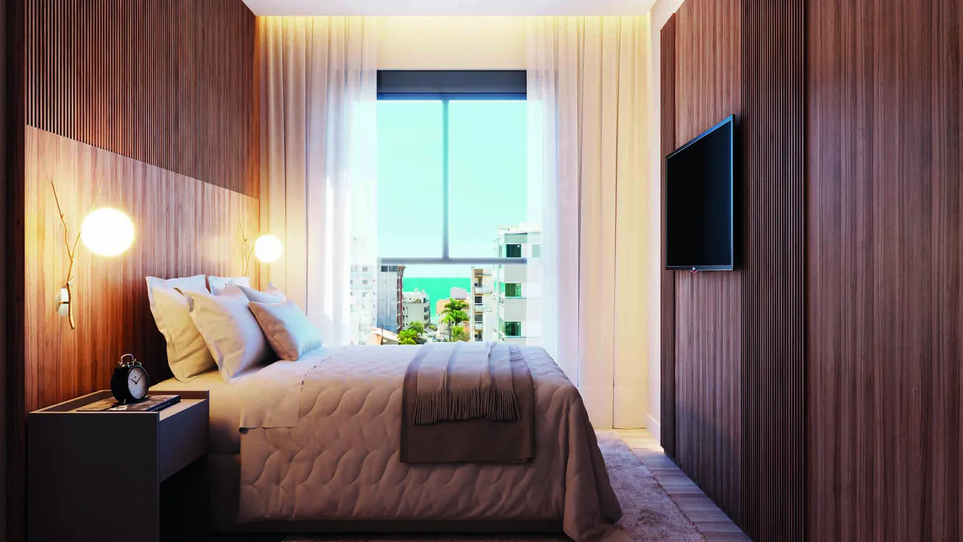 Suíte com painel de madeira na cabeceira, cama de casal, arandelas de leitura e janela com vista para o mar entre os prédios