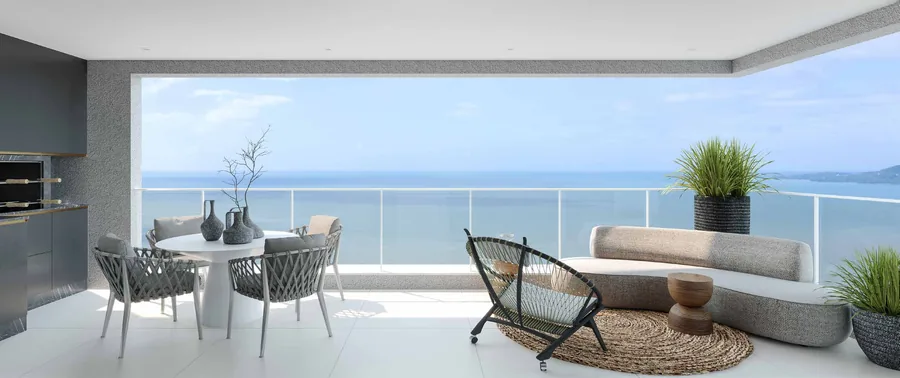 Varanda do apartamento tipo, com mesa de jantar, poltronas e vista aberta para a orla