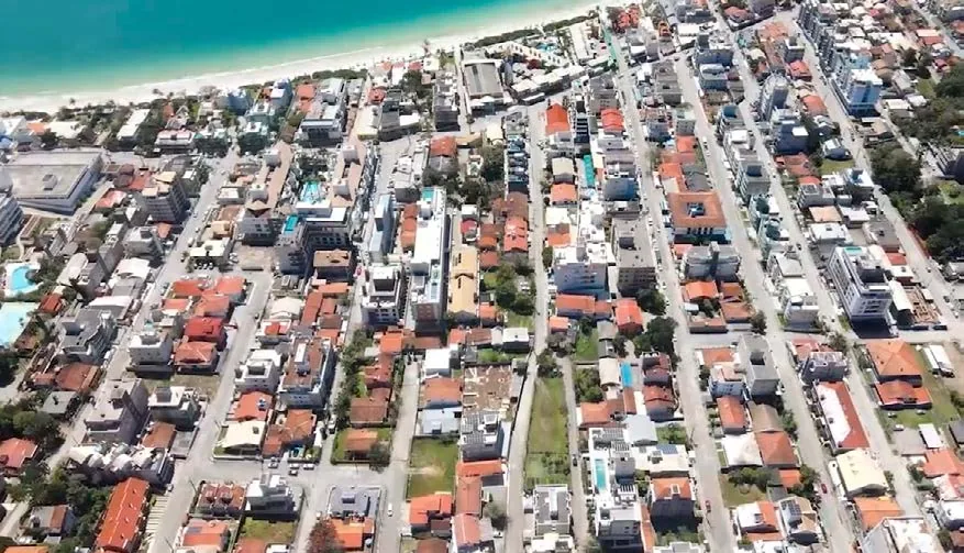 Vista aérea do Centro de Bombinhas, com as quadras baixas de casas e prédios e a faixa de areia ao fundo
