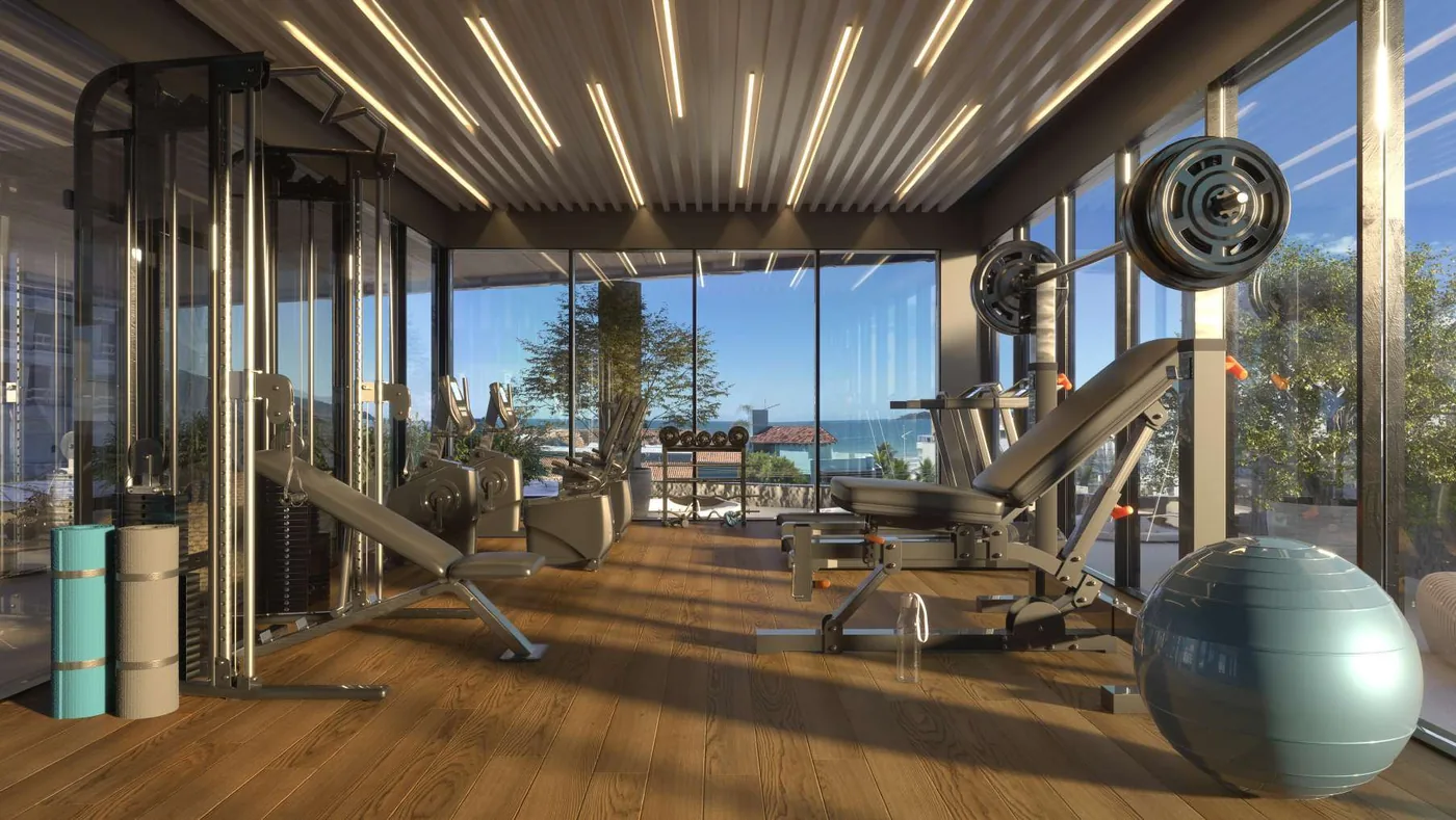 Academia com aparelhos de musculação alinhados diante das janelas, piso de madeira, bolas de pilates e a praia do lado de fora