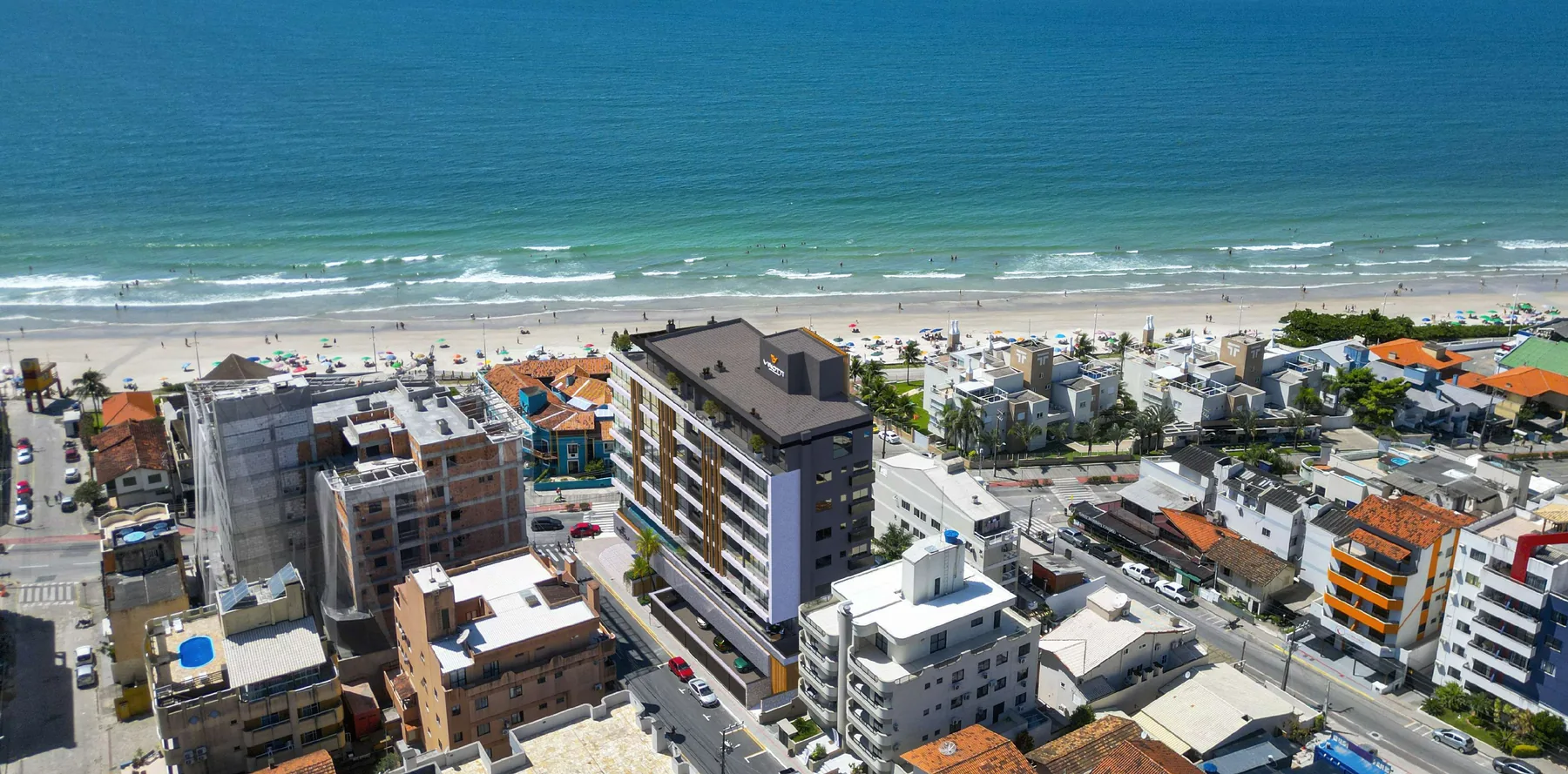 Vista aérea do quarteirão do Miraj, com o prédio entre as casas baixas do bairro, a faixa de areia e o mar logo adiante