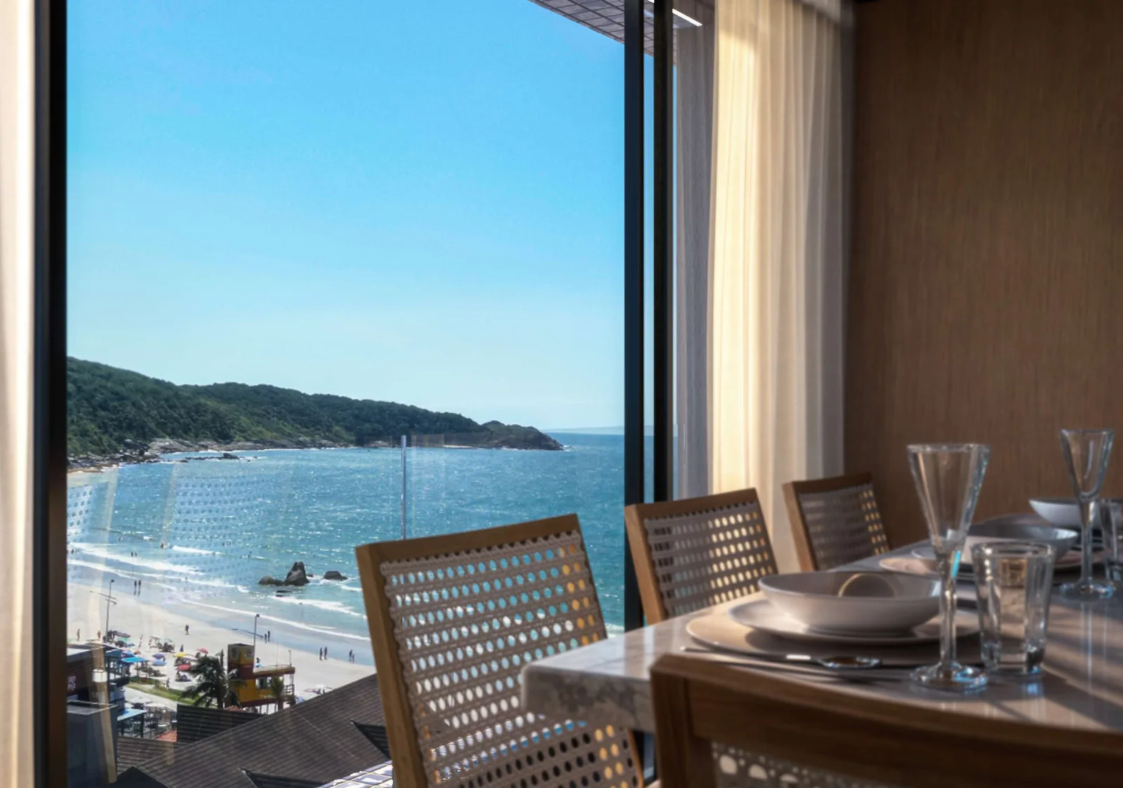 Living do T-04 visto do jantar, com mesa posta em primeiro plano, cadeiras de palhinha e a janela do piso ao teto para o mar e o costão