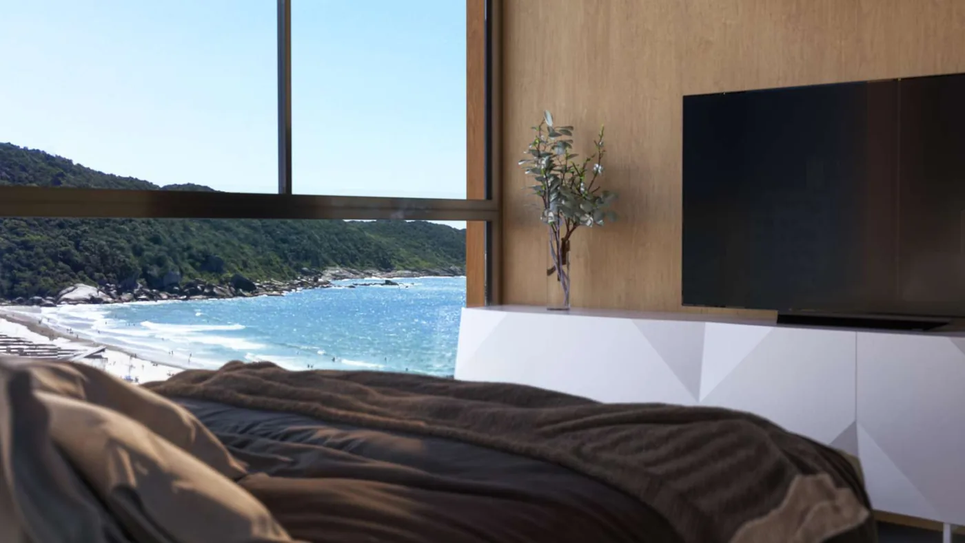 Suíte do T-03, com cama baixa de frente para a janela e, do lado de fora, o costão verde e a arrebentação