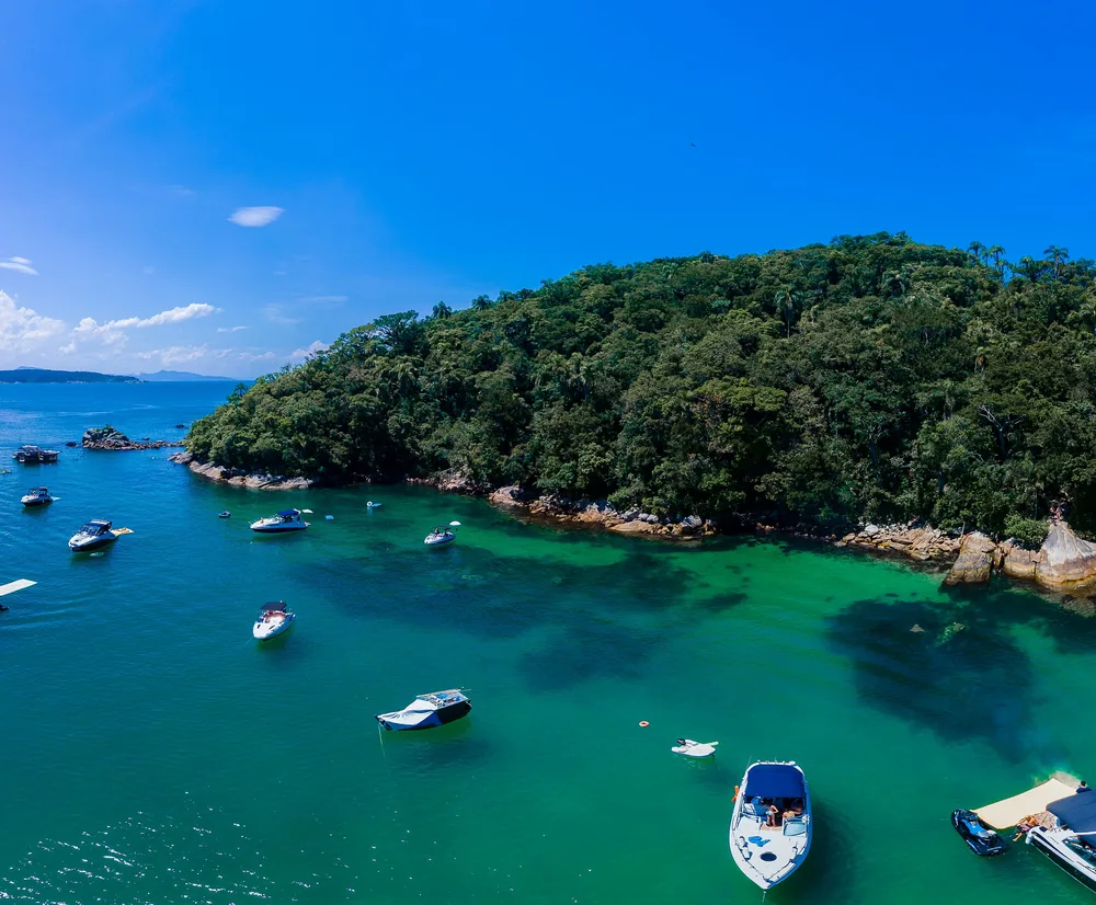 Enseada de Bombinhas vista do alto, com água azul-esverdeada, barcos fundeados e uma ilha coberta de mata