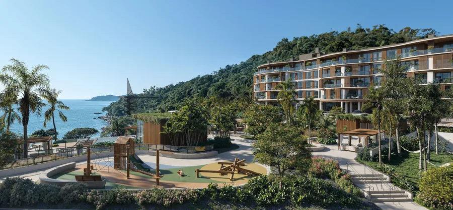 Praça de lazer central com playground, caminhos de pedra e paisagismo denso, com o mar ao fundo