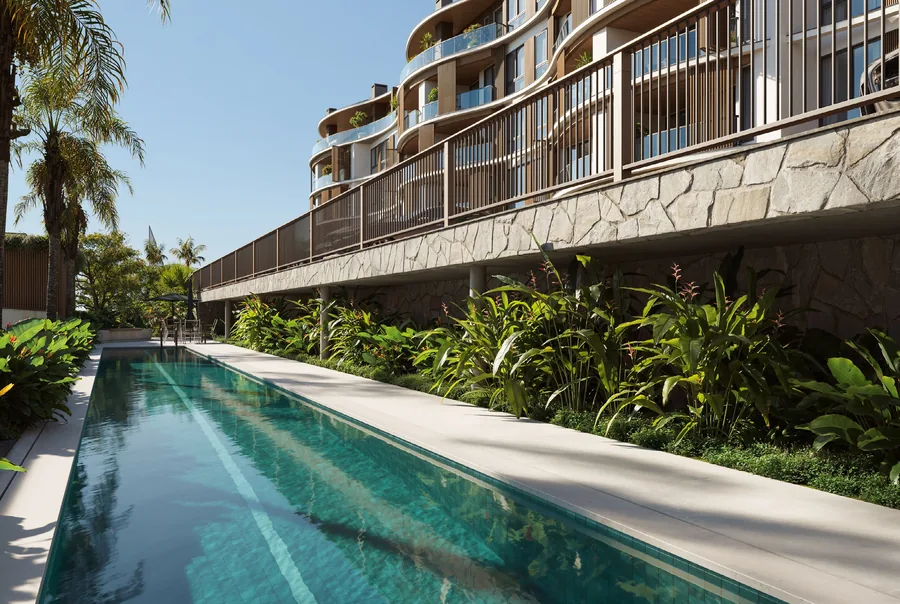 Piscina com raia semiolímpica margeada por vegetação densa, com a fachada do edifício ao fundo