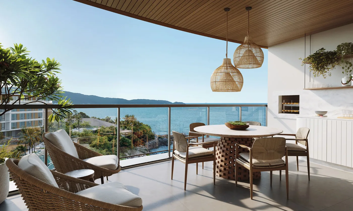 Varanda gourmet de apartamento, com mesa redonda para seis, poltronas, churrasqueira embutida e vista aberta para o costão e o mar