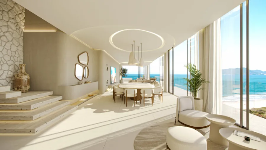 Sala de jantar integrada ao living, com mesa redonda, revestimento de pedra e janelas para o mar