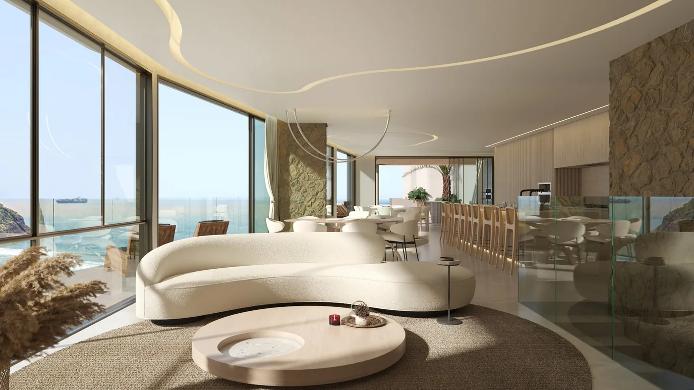 Living de apartamento com sofá curvo claro, mesa de centro redonda e parede de vidro aberta para o mar