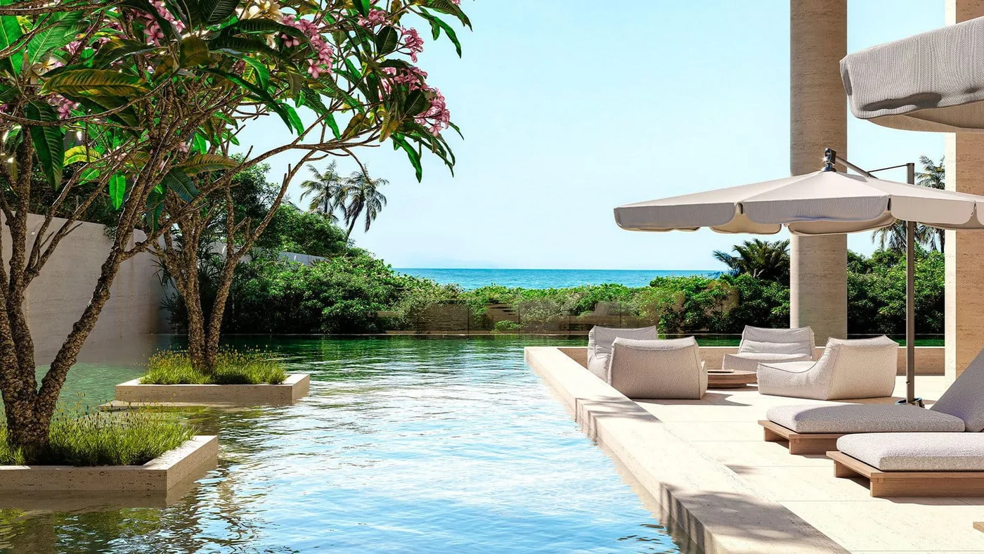 Piscina com espreguiçadeiras sob guarda-sóis, cercada de vegetação, com o mar logo adiante