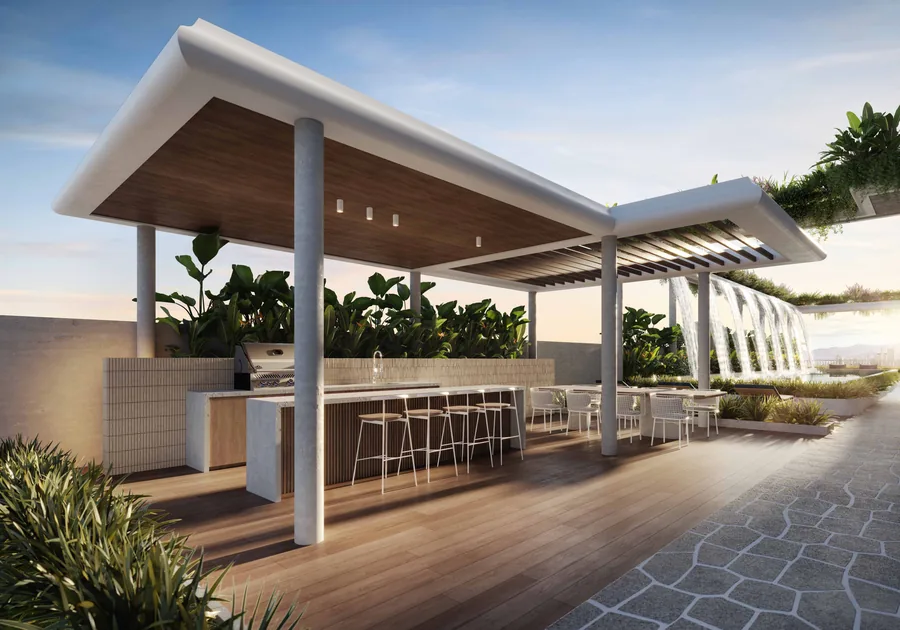 Espaço gourmet externo coberto por uma laje de madeira, com bancada, banquetas altas e vegetação em volta