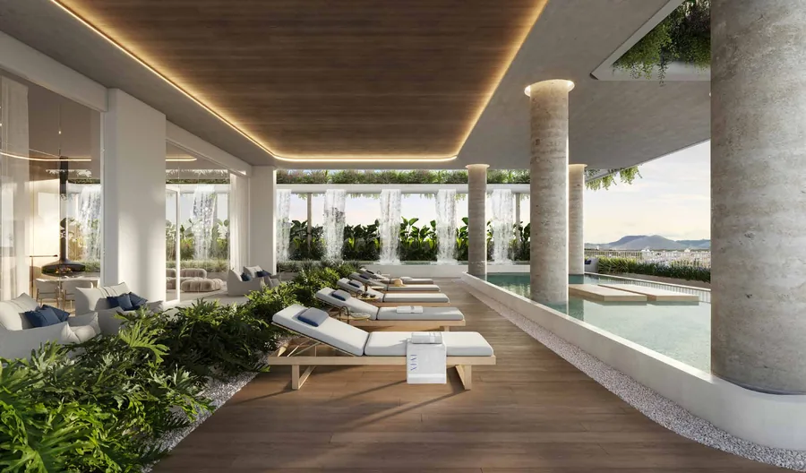 Deck da piscina com espreguiçadeiras brancas em fila, pilar roliço iluminado e vegetação densa na borda