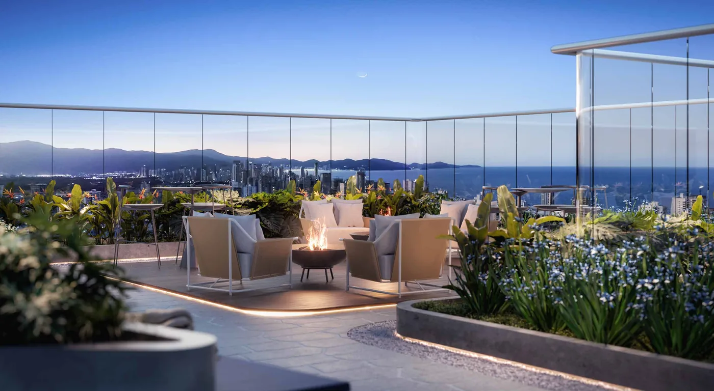 Praça de fogo no rooftop ao anoitecer, com poltronas em volta do braseiro, jardim florido e os morros da costa no horizonte
