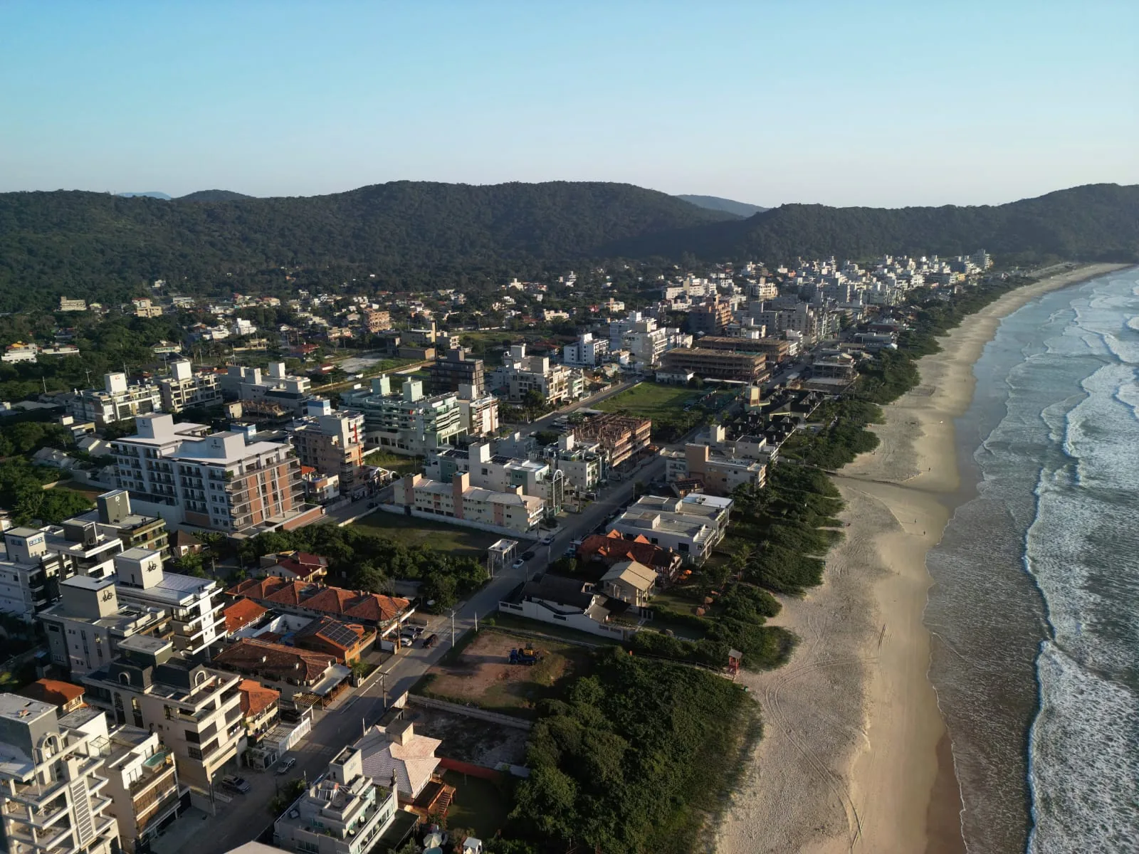 Vista aérea de Canto Grande, com a faixa de areia comprida de um lado, a arrebentação e o bairro de casas e prédios baixos do outro