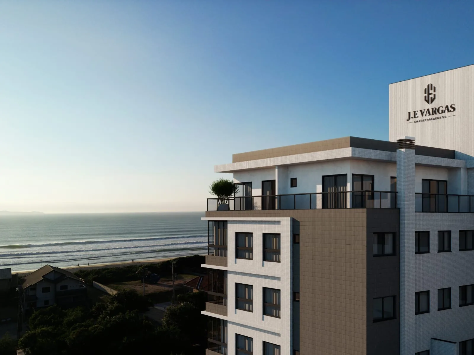 O topo do Villa Amoreira com a marca da J.E Vargas na empena, o mar e o costão de Canto Grande ao fundo