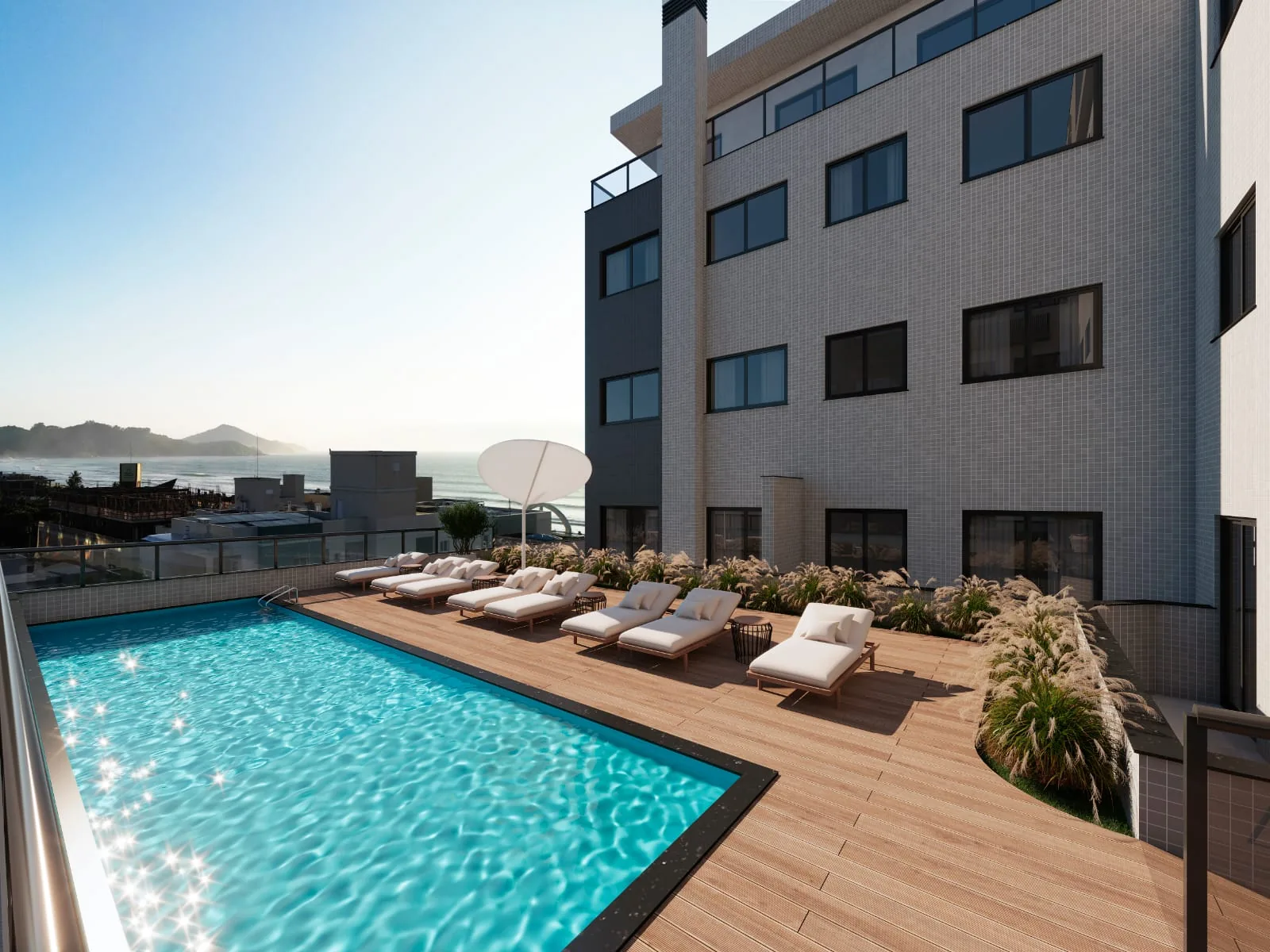 Piscina do Villa Amoreira com deck de madeira, espreguiçadeiras de um lado, canteiros na borda e o morro de Canto Grande ao fundo