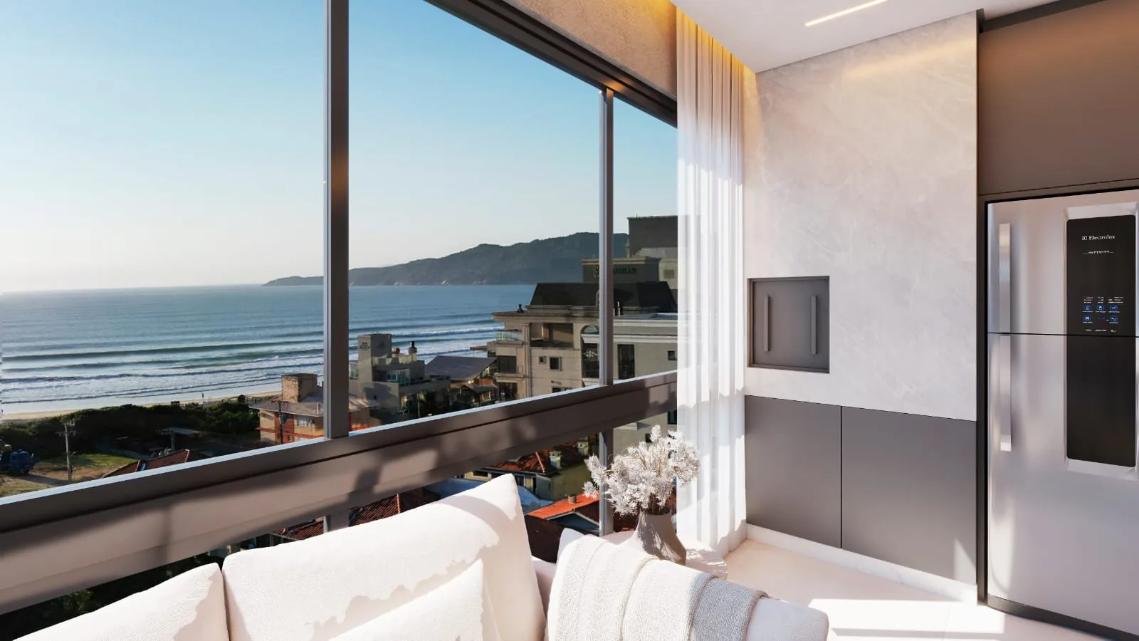 Sacada do apartamento tipo, com sofá branco junto ao vidro, a geladeira da cozinha ao lado e o mar e o costão de Canto Grande pela janela