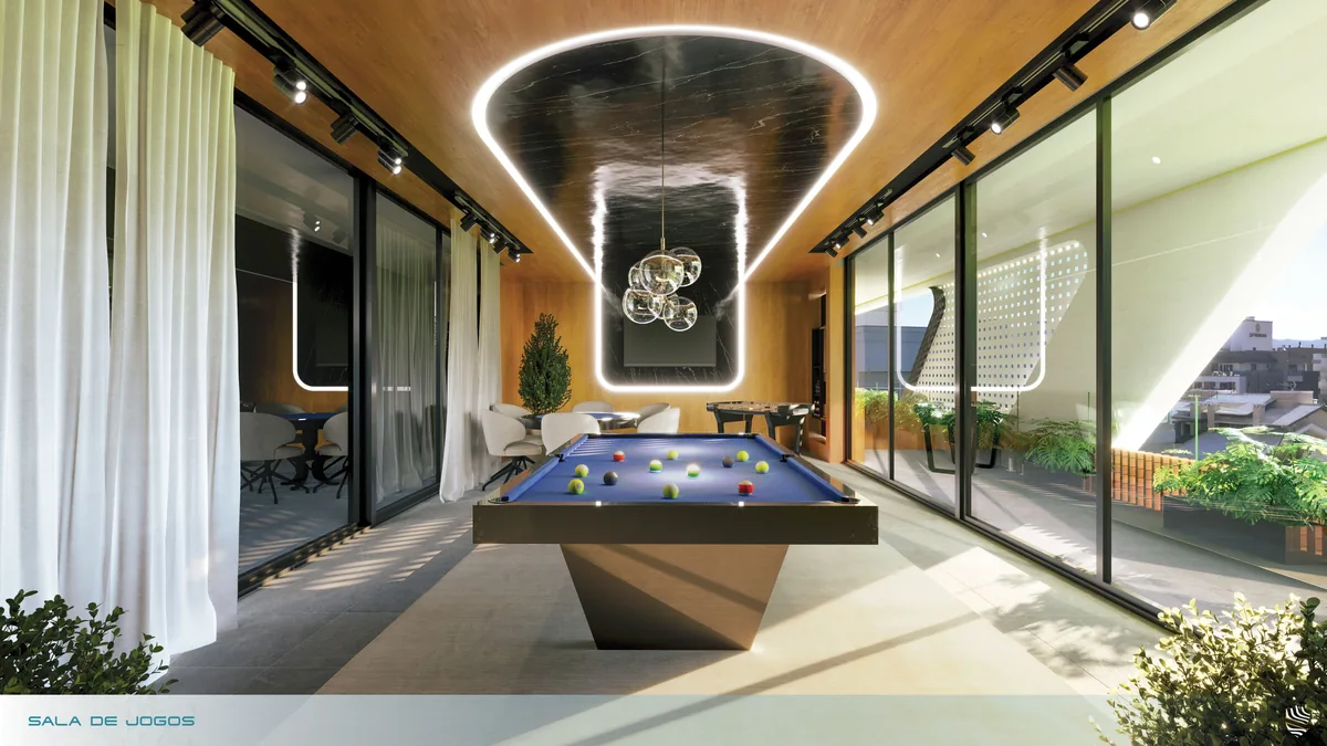Sala de jogos com mesa de sinuca ao centro, cortinas claras e janelas para a vegetação